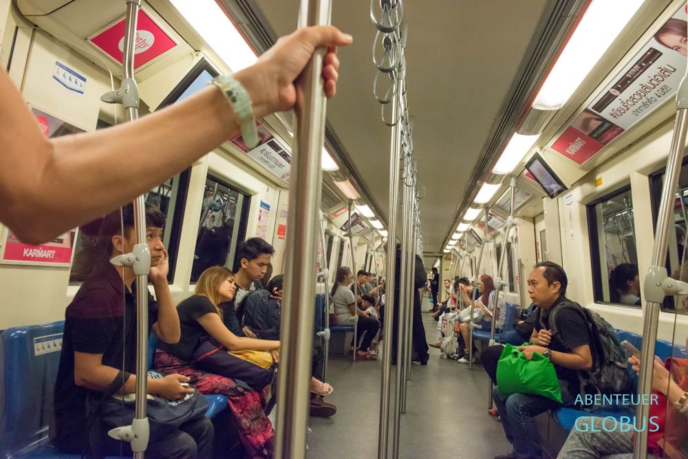 Fahrgastraum im BTS Skytrain in Bangkok mit Fahrgästen auf den Sitzbänken links und rechts sowie Haltestangen in der Mitte, Thailanden.