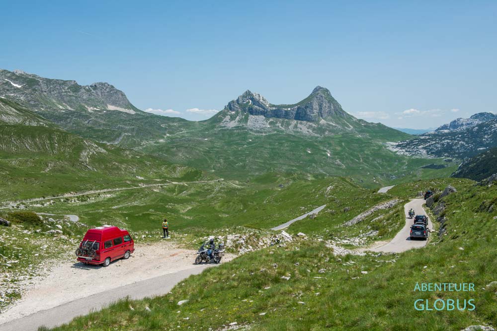 Roter Van, Motorradfahrer und Autos auf der Panoramastraße Durmitor Ring im Nationalpark Durmitor mit Berg Sedlena Greda (Saddle of Gods)