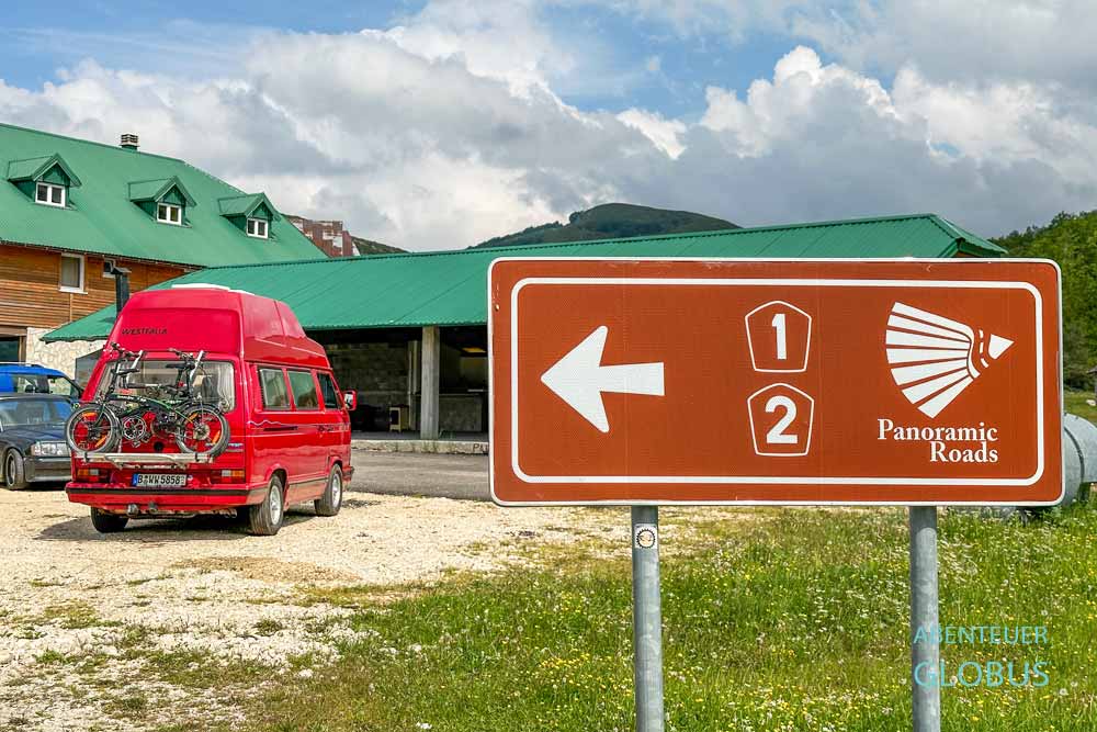 Schild der Panoramastraßen 1 und 2 des Durmitor-Rings mit einem roten Camper am Restaurant in Trsa im Nationalpark Durmitor, Montenegro.