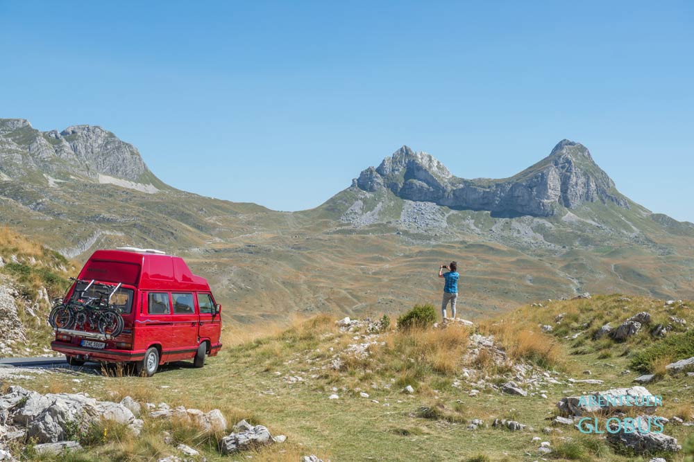 Roter Van mit fotografierender Frau im Vordergrund vor dem herbstlichen Bergmassiv Sedlena Greda (Saddle of Gods) im Durmitor-Nationalpark