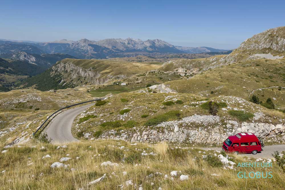 Ein rotes Wohnmobil fährt auf der Panoramastraße 2 des Durmitor-Rings im herbstlichen Durmitor-Nationalpark, Montenegro