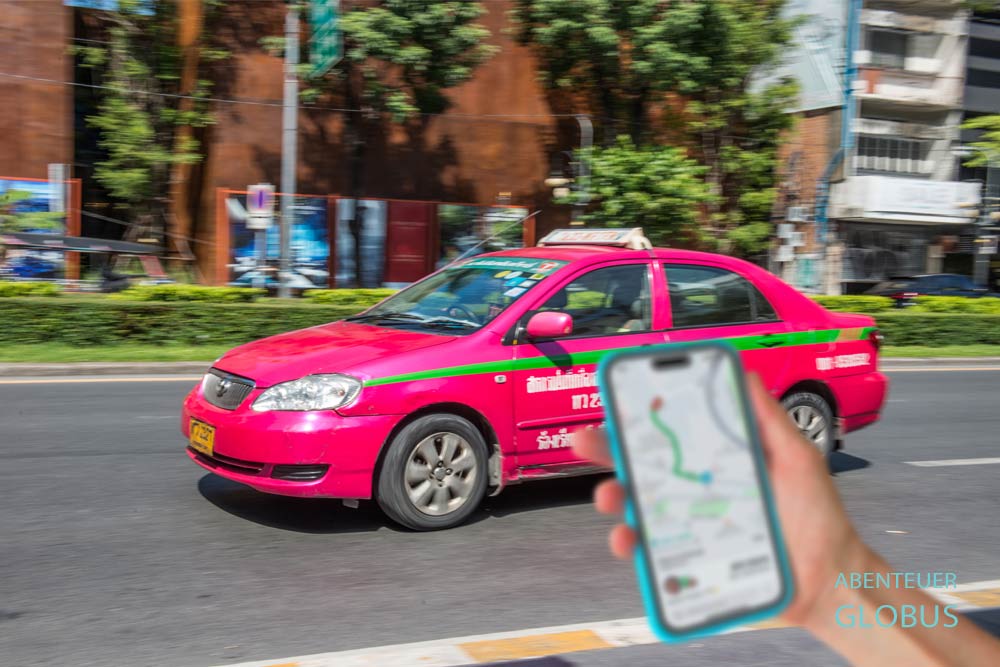 Hand hält ein Smartphone mit geöffneter Grab-Taxi-App, im Hintergrund ein fahrendes Taxi