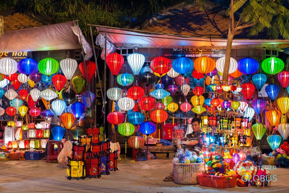 Verkäufer sitzt in einem Geschäft zwischen beleuchteten Lampions in Hoi An.