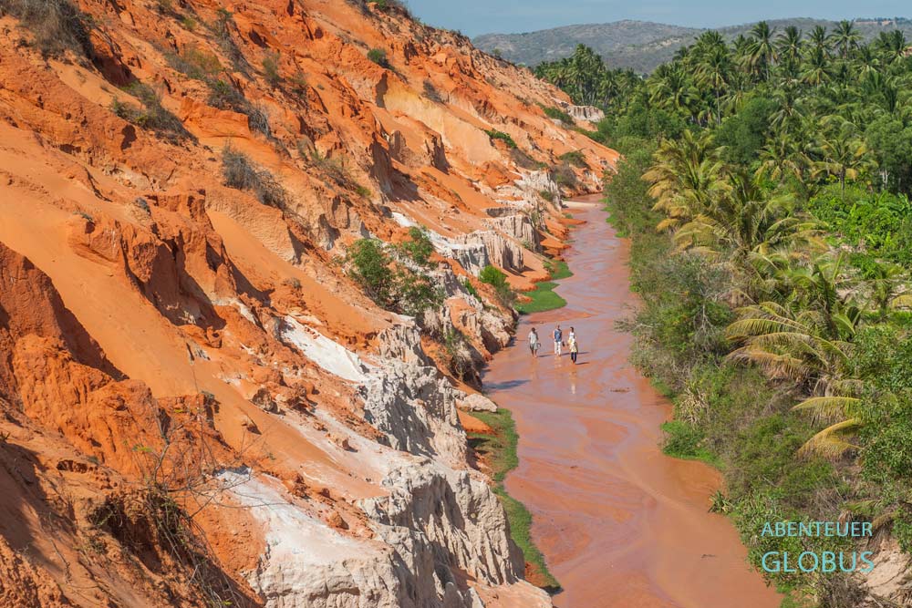 Menschen im braunen Fairy Stream zwischen orangefarbenen Sandformationen und Palmen