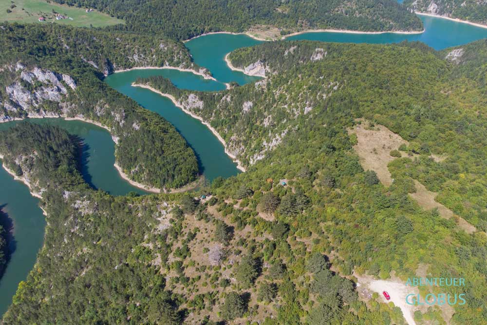 Der türkisblaue Fluss Ćehotina schlängelt sich durch die grüne Berglandschaft bei Pljevlja in Montenegro, unten rechts ein Parkplatz mit rotem Wohnmobil