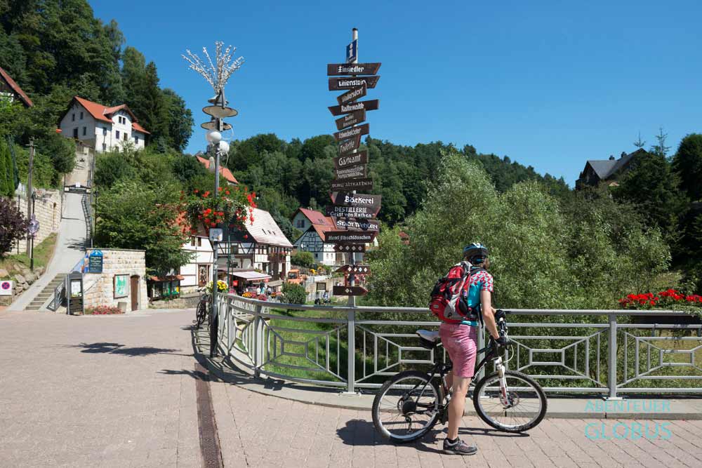Radfahrerin an Hinweisschildern auf dem Elberadweg in Rathen, Nationalpark Sächsische Schweiz