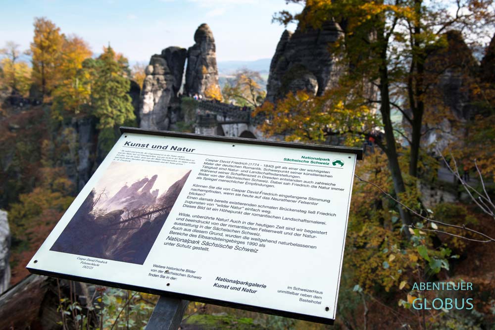 Schild am Malerweg mit der Basteibrücke im Hintergrund