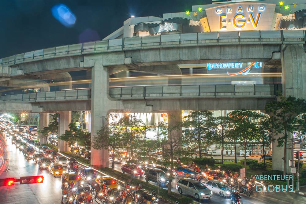 Stau und zähfließender Verkehr auf einer Straße in Bangkok, darüber das öffentliche Verkehrsmittel BTS Skytrain