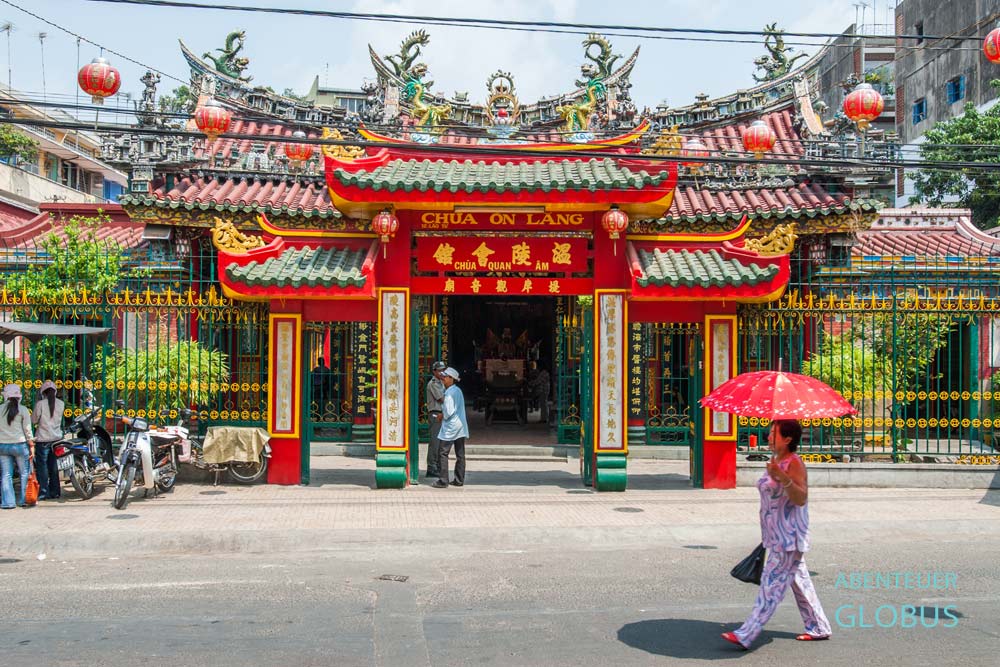 Chùa Ông Lăng Tempel, vor dem eine Frau mit rotem Sonnenschirm vorbeigeht