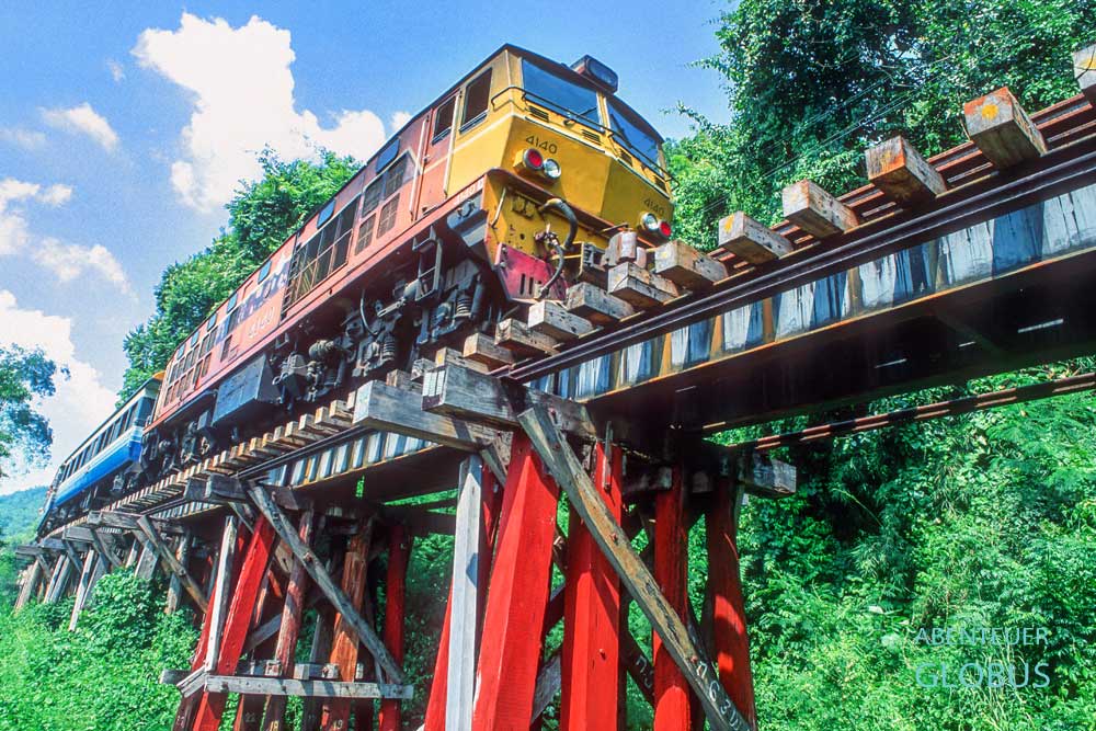 Blick von unten auf einen Zug der Thailand-Burma-Death-Railway, der über das Wang Po Viadukt bei Kanchanaburi in Thailand fährt.
