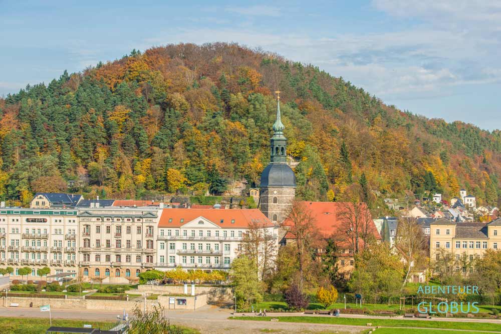 Hotel Elbresidenz an der Therme und Johanniskirche im Kurort Bad Schandau vor einem Berg mit Herbstwald