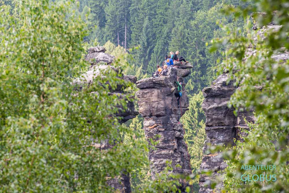 Kletterer auf Felssäule im Bielatal, umgeben von Felsen und Bäumen im Elbsandsteingebirge