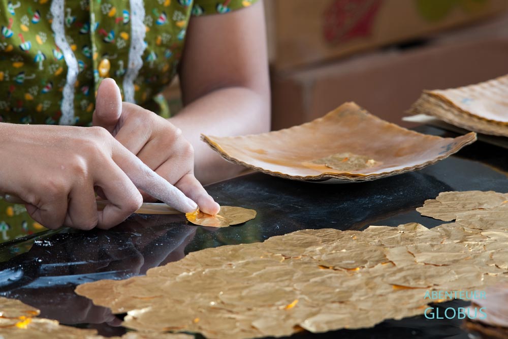 Frauenhände sortieren hauchdünne Goldplättchen in einer Blattgoldmanufaktur in Mandalay, Myanmar.