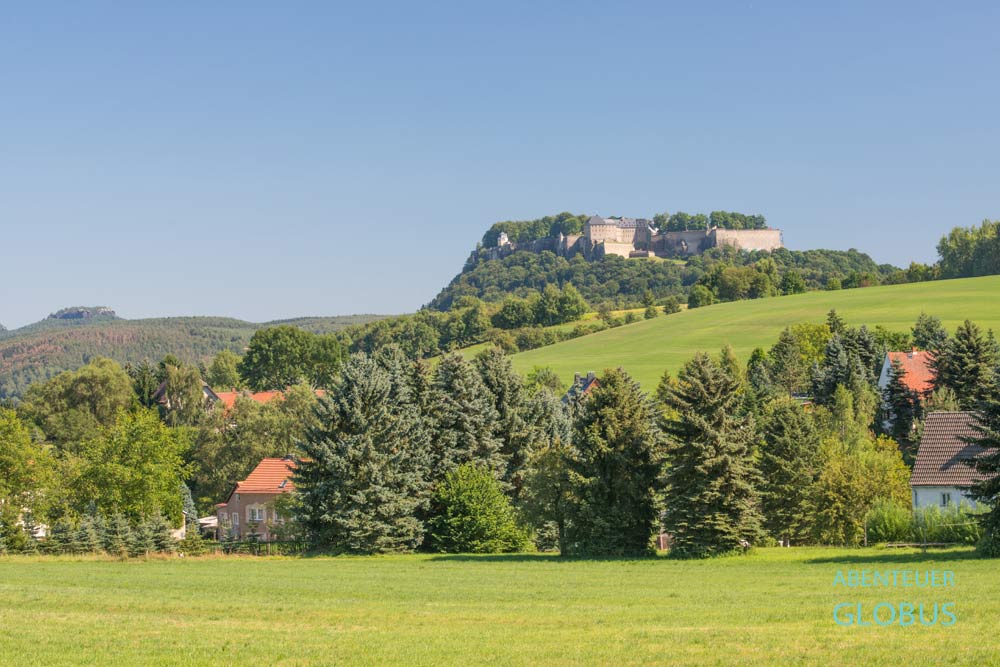 Häuser zwischen Bäumen, dahinter Festung Königstein am Malerweg bei Königstein im Elbsandsteingebirge