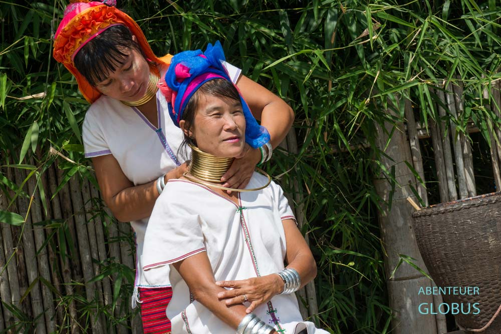 Eine Padaung-Frau hilft einer anderen Frau, den Messing-Halsring im Dorf Panpet, Myanmar, abzunehmen