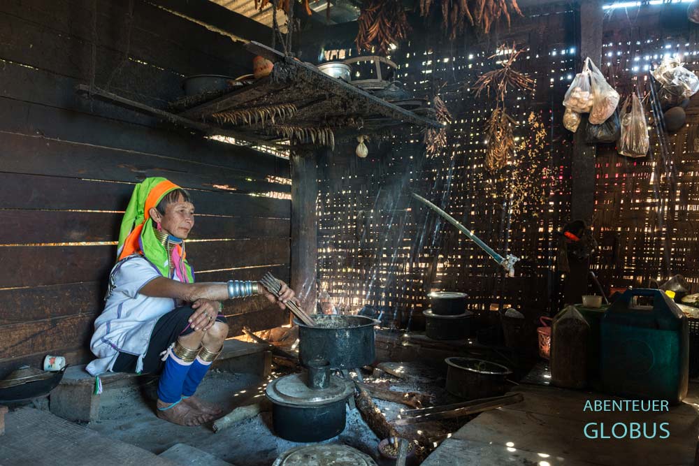 Padaung-Frau in traditioneller Kleidung an der Kochstelle im Haus im Dorf Panpet, Myanmar.