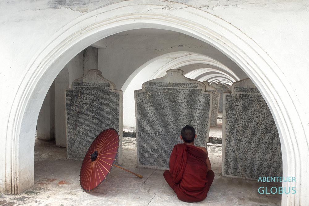 Lesender Mönch mit rotem Bambusschirm vor einer Marmortafel der Kuthodaw-Pagode in Mandalay, Myanmar