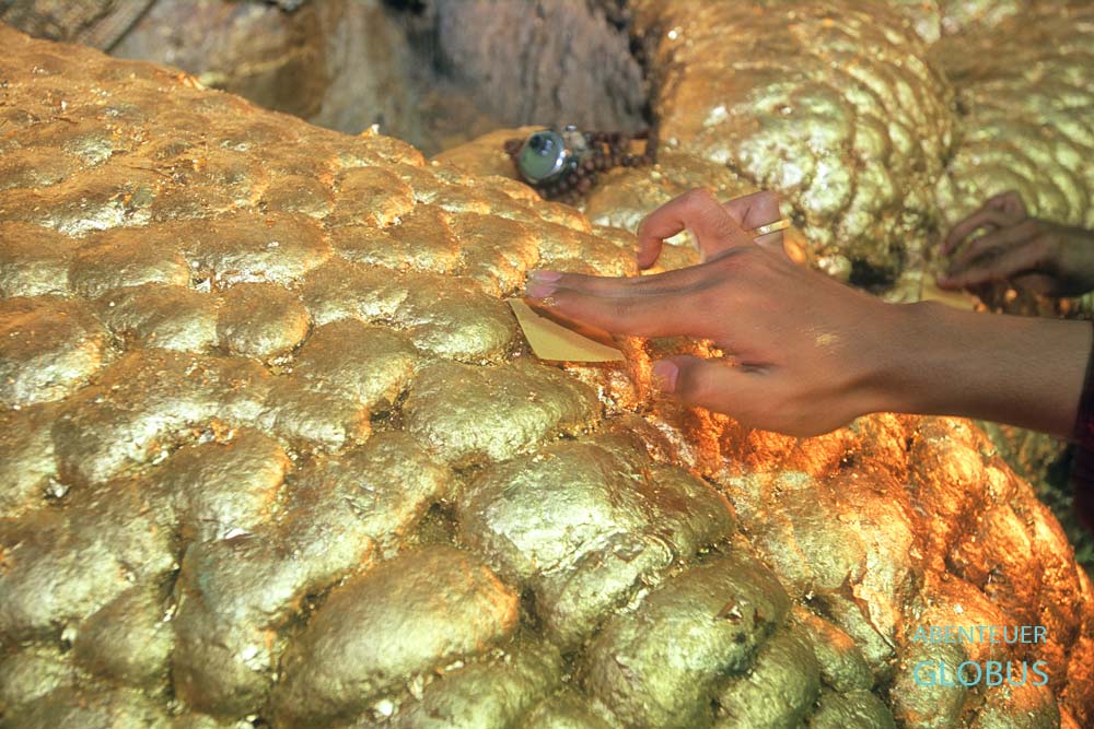 Männerhand bringt Goldplättchen auf die vergoldete Oberfläche des Mahamuni-Buddhas in Mandalay, Myanmar.