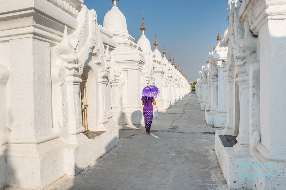 Frau mit lila Schirm zwischen den weißen Stupas der Kuthodaw-Pagode in Mandalay, Myanmar.
