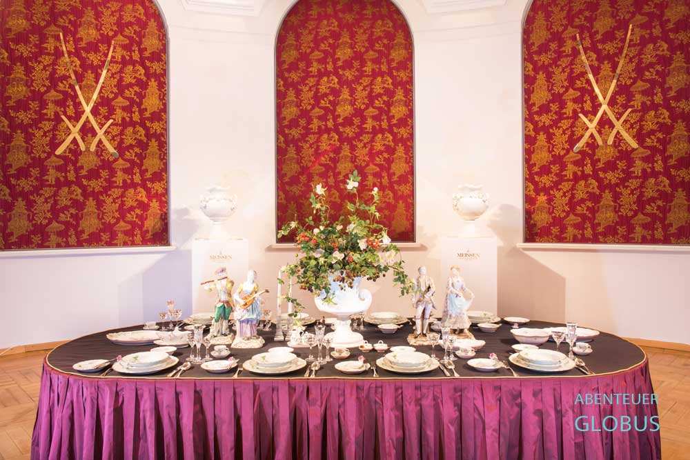 Im Vordergrund gedeckter Tisch mit edlem Porzellan im Museum „Erlebniswelt Meissen“ der Staatlichen Porzellan-Manufaktur Meissen, an der Wand die zwei Schwerter, das Markenzeichen