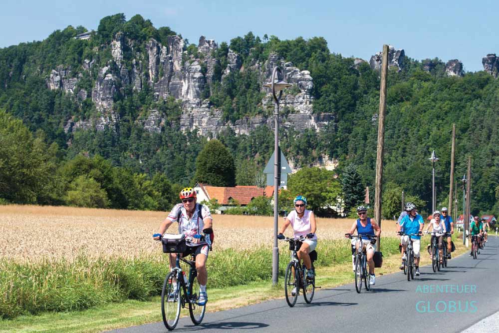 Radfahrergruppe auf dem Elberadweg in Rathen, dahinter das Felsmassiv Bastei im Nationalpark Sächsische Schweiz