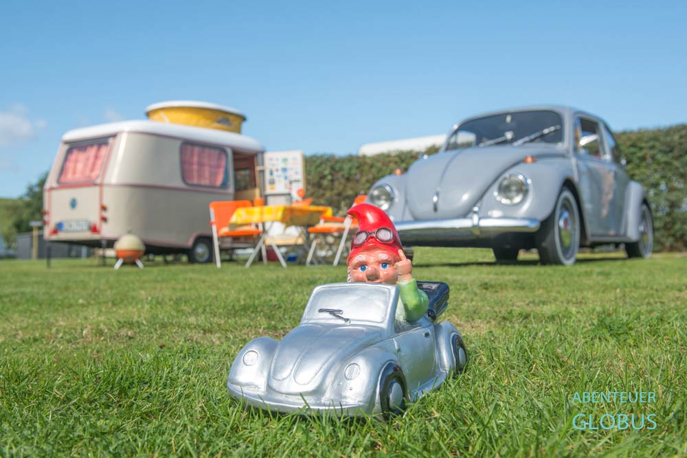 Gartenzwerg im VW Käfer, dahinter Oldtimer VW Käfer und Wohnwagen Eriba Puck auf einem Campingplatz