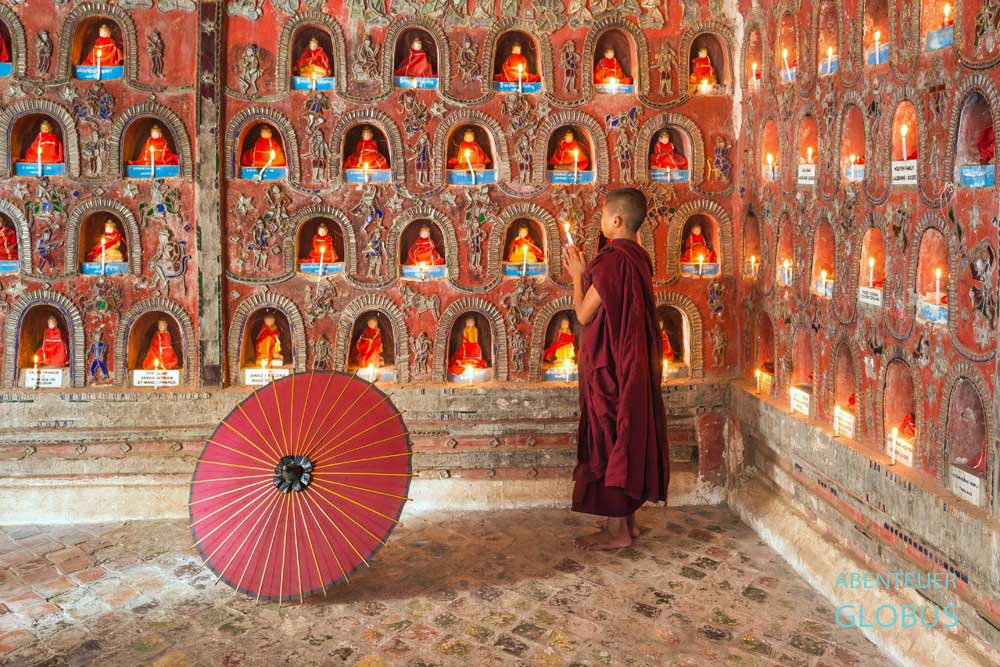 Mönch mit rotem Bambusschirm betet vor Buddha-Statuen im Shwe Yan Bye Kloster am Inle-See.