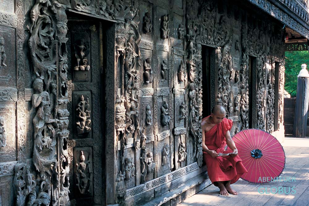 Lesender Mönch mit rotem Bambusschirm auf der Terrasse des Shwenandaw-Klosters in Mandalay