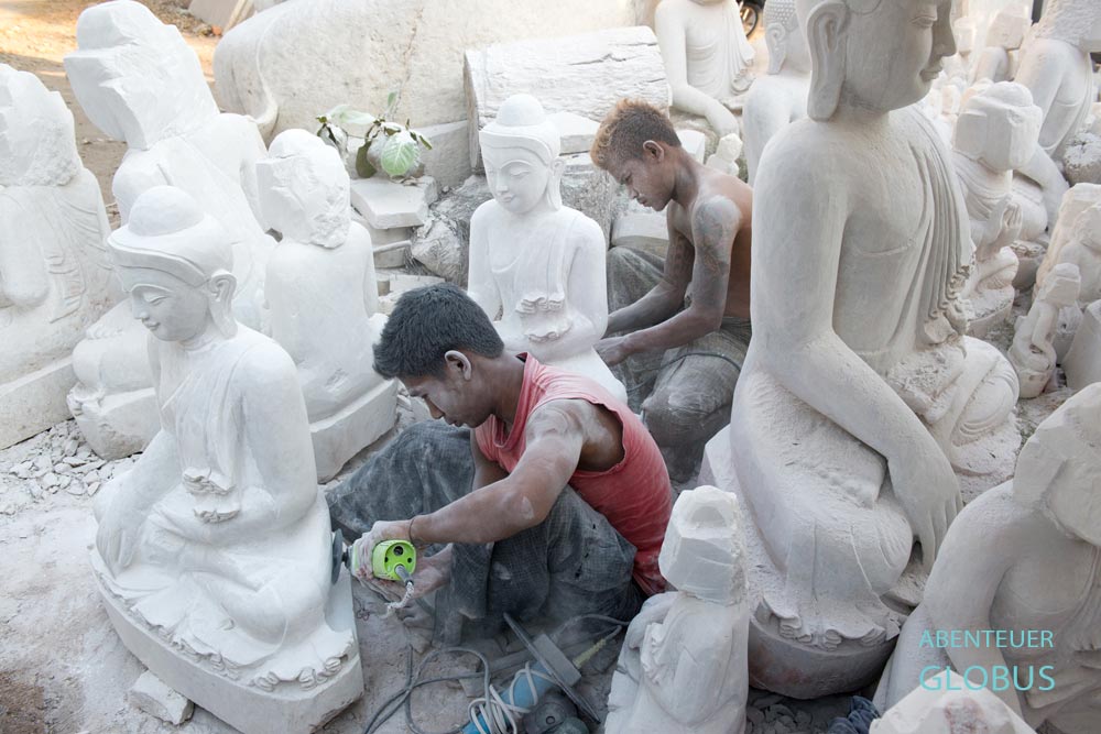 Zwei Steinmetze schleifen weiße Buddha-Statuen aus Marmor in einer Werkstatt in Mandalay, Myanmar.