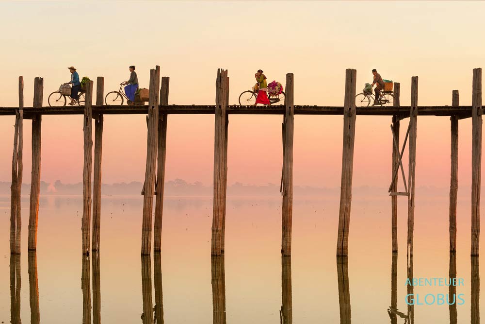 Frauen auf Fahrrädern auf der U-Bein-Brücke im Morgenlicht in Amarapura, Myanmar.