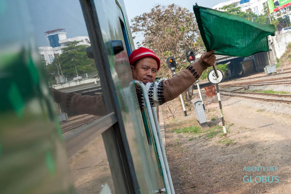 Zugbegleiter schwenkt eine grüne Fahne zur Abfahrt des Yangon Circle Line in Yangon