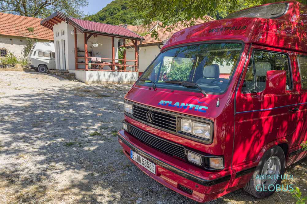 Roter Camper, dahinter Sanitärhaus vom Padma Moon Camp in Visoko