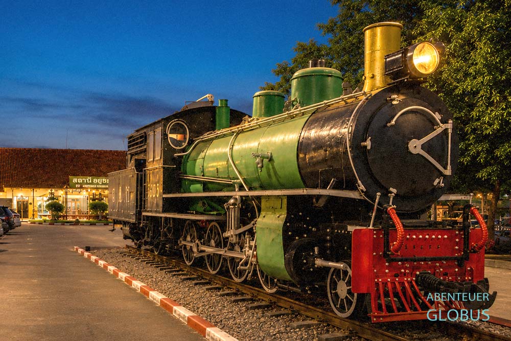 Historische Dampflokomotive als Denkmal vor dem beleuchteten Bahnhof in Chiang Mai bei Nacht.