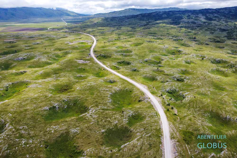Straße durch die grüne Landschaft mit Dolinen im Frühling zwischen Rama-See und Livno