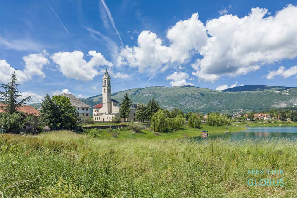 Grüne Wiese mit Blick auf das Franziskanerkloster Rama-Scit mit der Kirche Maria Himmelfahrt auf der Halbinsel Scit im Rama-See