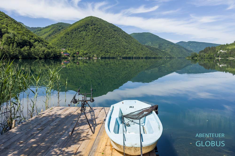Steg mit Angeln und Boot am Großen Plivsko Jezero, umgeben von grünen Bergen in Jajce
