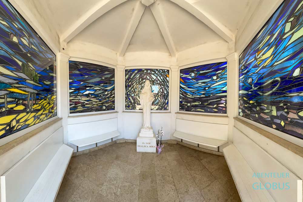 Die weiße Skulptur der Mutter Gottes und farbenfrohe Glasfenster schmücken die Kapelle des Lebens in Medjugorje.