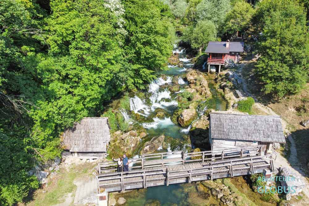 Zwei Besucher auf der Holzbrücke an den Krupa Wasserfällen und alte Holzmühlen am Fluss Krupa in Krupa na Vrbasu
