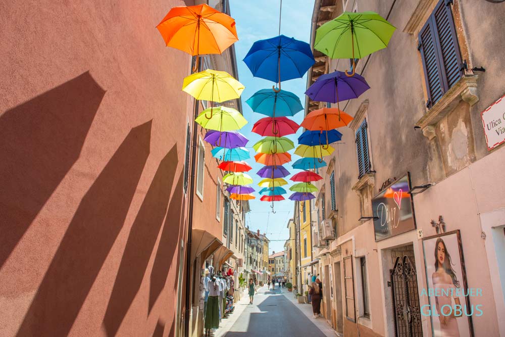 Gasse Ulica Gradska Vrata mit bunten Schirmen in Novigrad auf der Halbinsel Istrien in Kroatien
