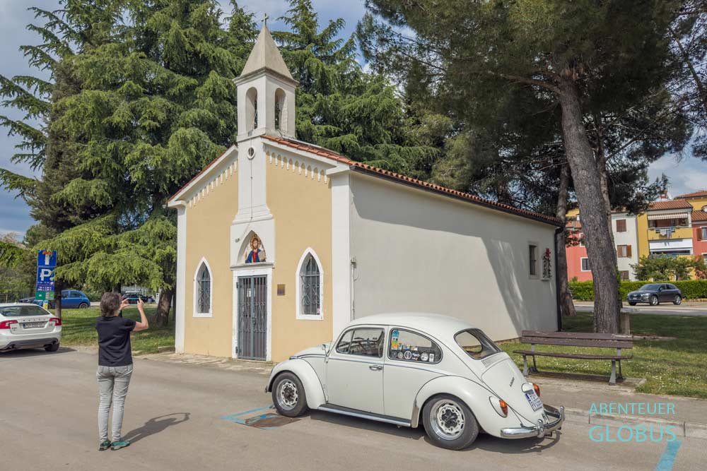 Frau fotografiert cremefarbenen Oldtimer VW Käfer vor der Kirche des Heiligen Antonius (Crkva Sv. Ante) in Novigrad.