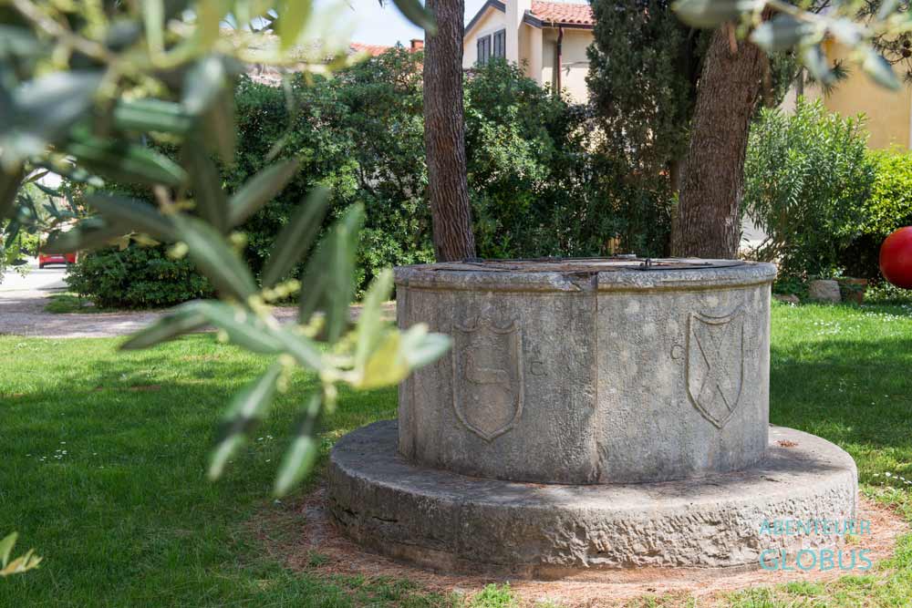 Pozzo Novo Brunnen aus Steinplatten mit alten Wappen auf einer Wiese in Novigrad, Kroatien