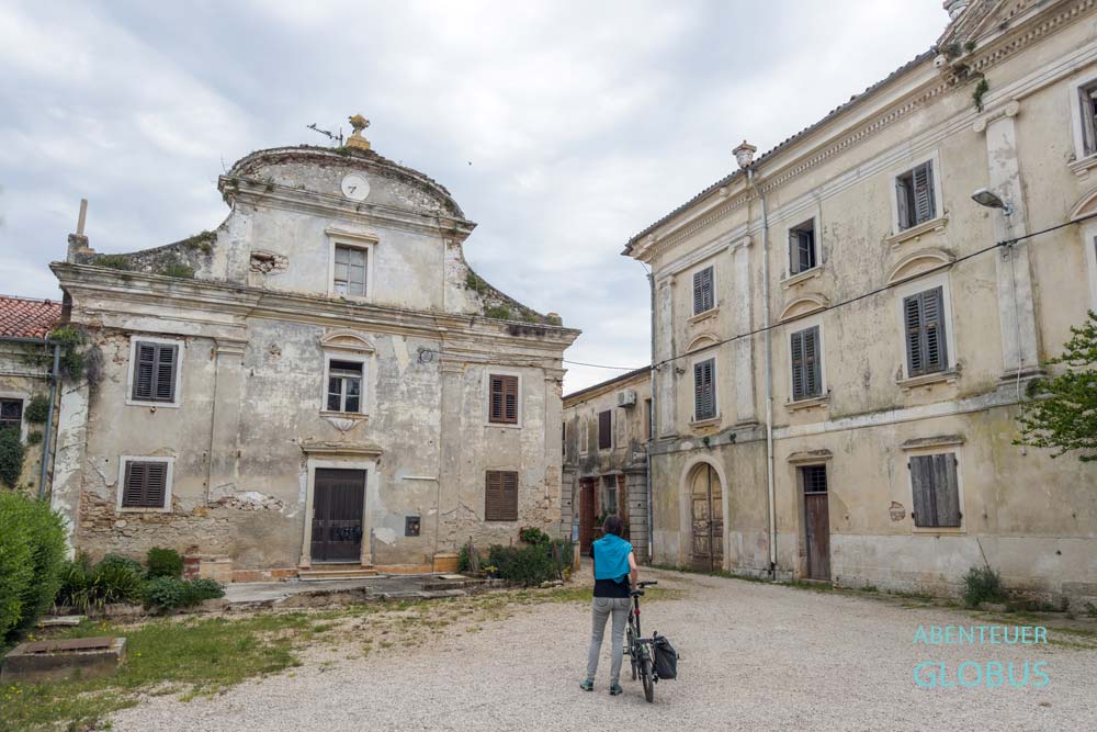 Radfahrerin vor zwei Gebäuden des Landgutes bzw. Klosters in Dajla nahe Novigrad in Kroatien