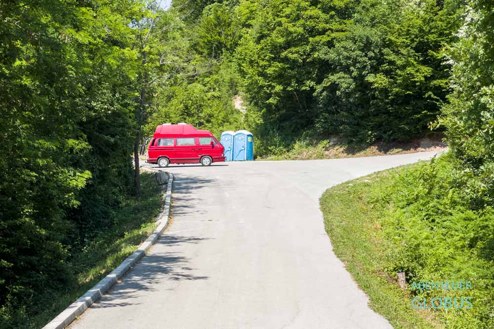 Roter Campervan auf dem Parkplatz mit zwei blauen Dixis am Wasserfall Blihe bei Sanski Most
