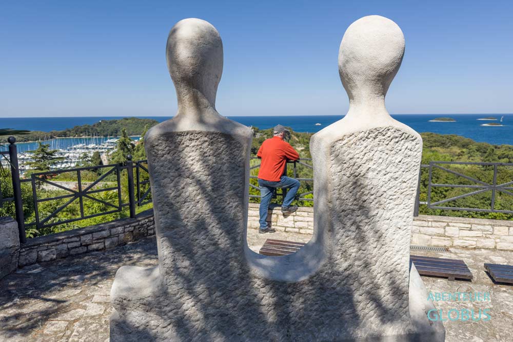 Mann zwischen zwei Steinskulpturen am Aussichtspunkt Bepo & Tonina in der Altstadt von Vrsar in Istrien