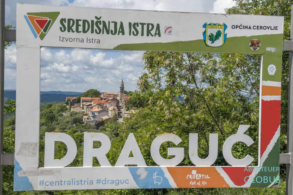 Rahmen mit Schriftzug Draguc im Vordergrund, der Ort Draguc dahinter, in Istrien