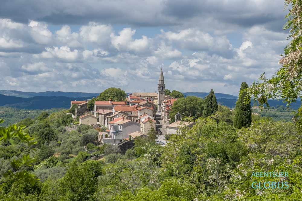 Dorf Draguc mit Häusern und Glockenturm der Heiligenkreuzkirche auf einem schmalen Hügelkamm in Istrien