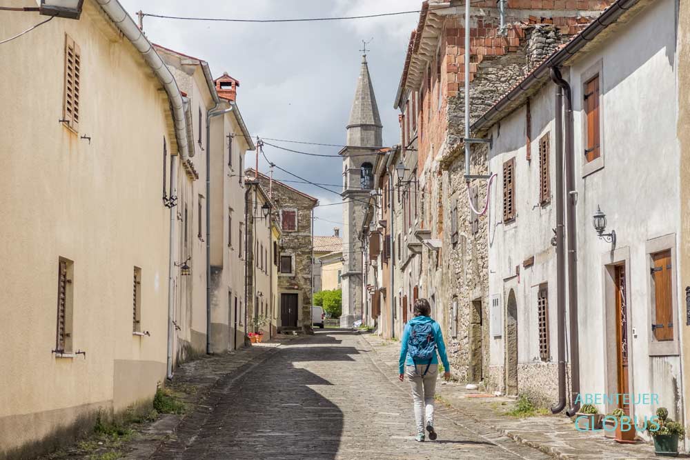 Besucherin in der Hauptgasse von Draguc, gesäumt mit Steinhäusern, im Hintergrund der Campanile der Heiligenkreuzkirche, Istrien in Kroatien