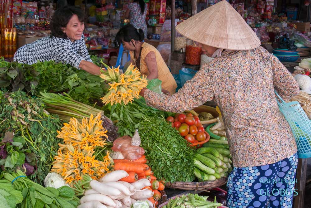 Vietnamesische Frau mit Strohhut kauft Kräuter und Gemüse auf einem Markt in Vietnam.