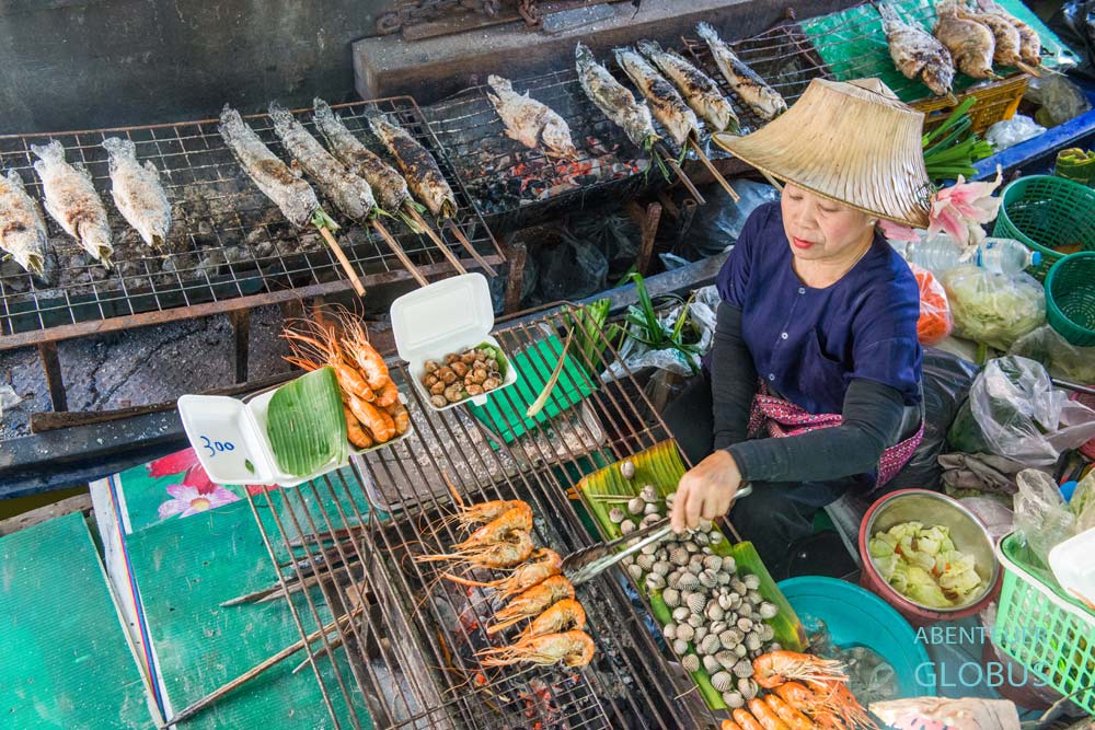 Eine Frau grillt Shrimps auf einem Boot auf dem schwimmenden Markt Taling Chan in Bangkok.