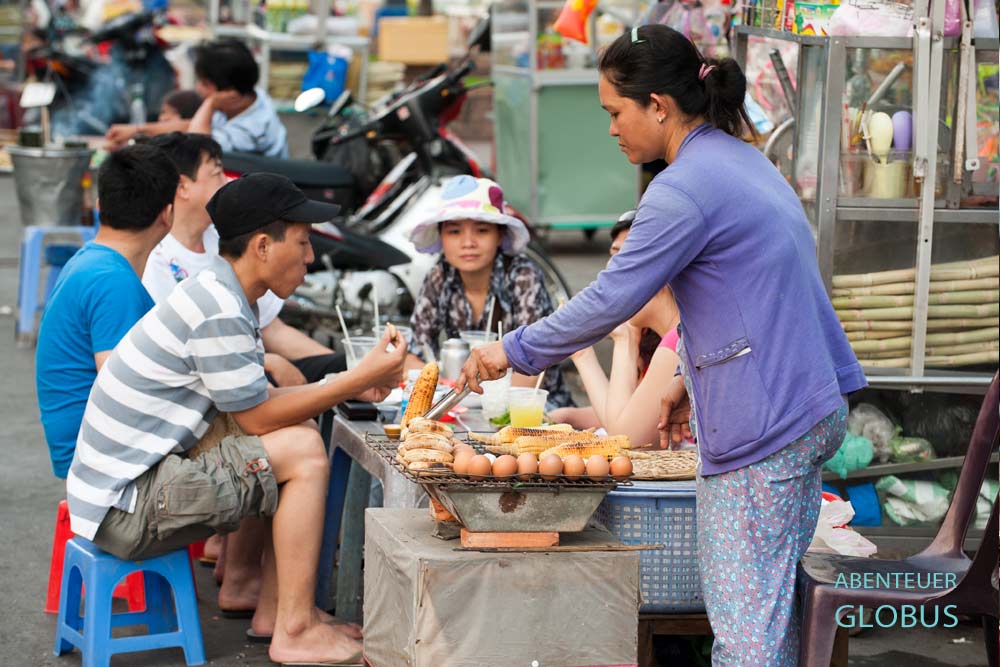 Streetfood-Stand in Vietnam, an dem Gäste auf kleinen Hockern sitzen und essen.